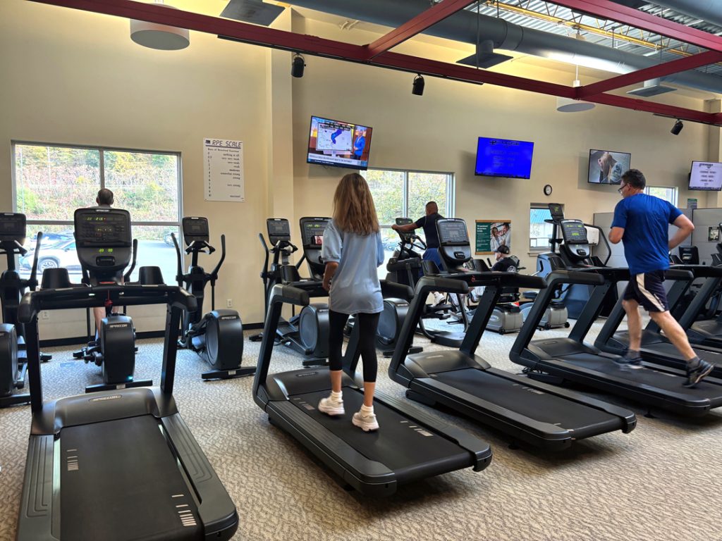 Several people exercise on treadmills and elliptical machines inside a gym.